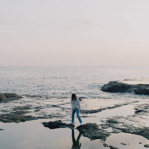 person-stands-on-rocks-poking-out-of-the-ocean-shoreline